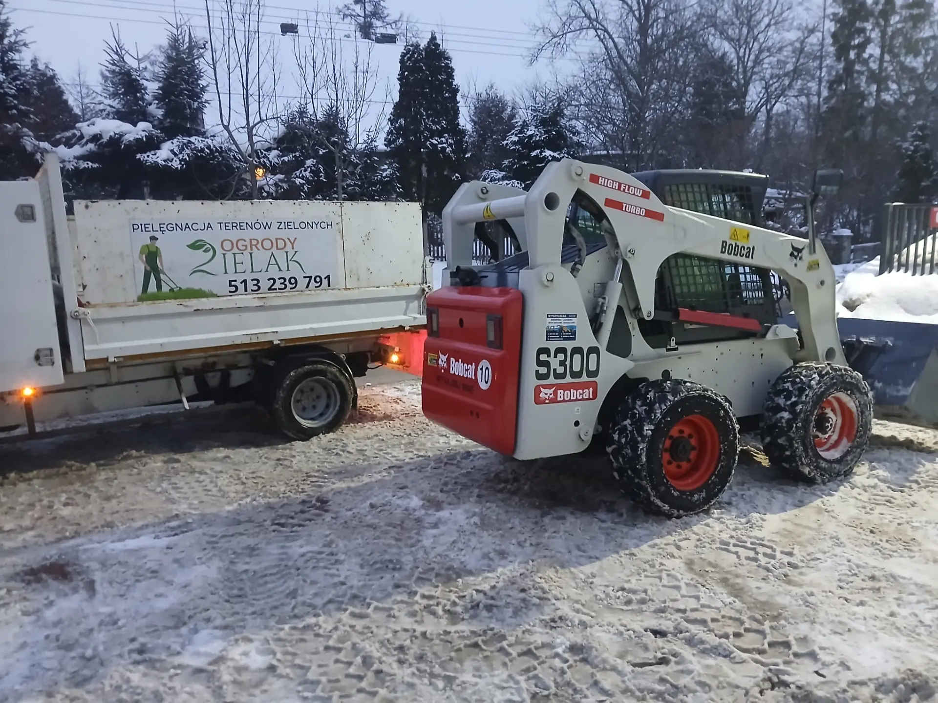 Ładowarka Bobcat odśnieżająca teren i ładująca śnieg na samochód firmy Ogrody Zielak