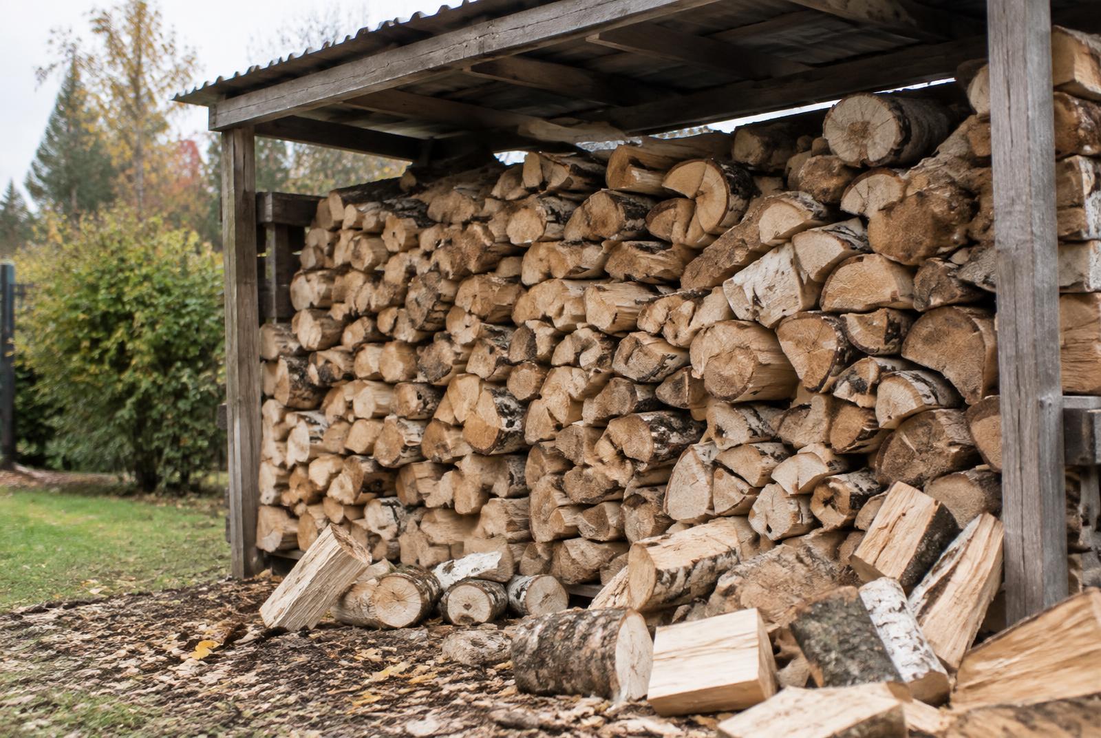 Sezonowane drewno kominkowe ułożone pod drewnianą wiatą